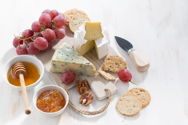 Gjuten ostar, frukt och snacks på en vit trä bakgrund — Stockfoto