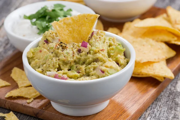 Omáčkou guacamole, tomatová salsa a kukuřičnými chipsy na dřevěném prkénku — Stock fotografie