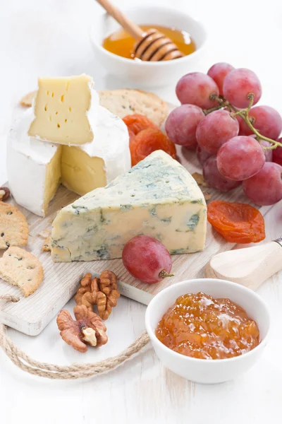 Lisované sýry, ovoce a občerstvení na bílém pozadí, dřevěné — Stock fotografie