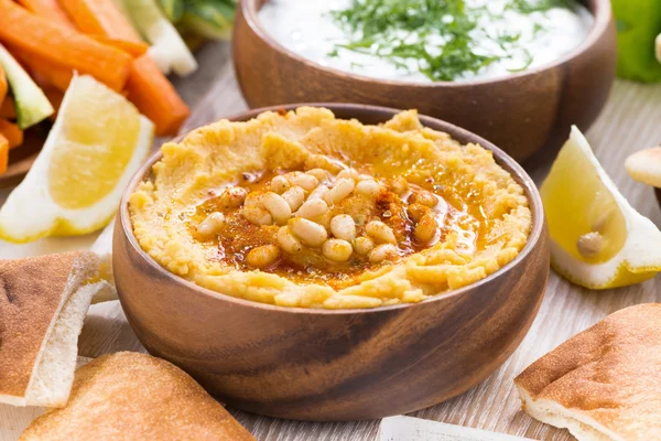 Хумус в деревянной миске с пита-хлебом и свежими овощами — стоковое фото