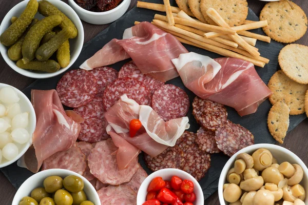 Snacks de carne delicatessen, salchichas y encurtidos en una pizarra, vista superior — Foto de Stock