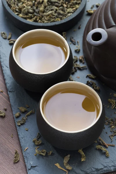 Teapot and cups with green tea on black background, top view — Stock Photo, Image