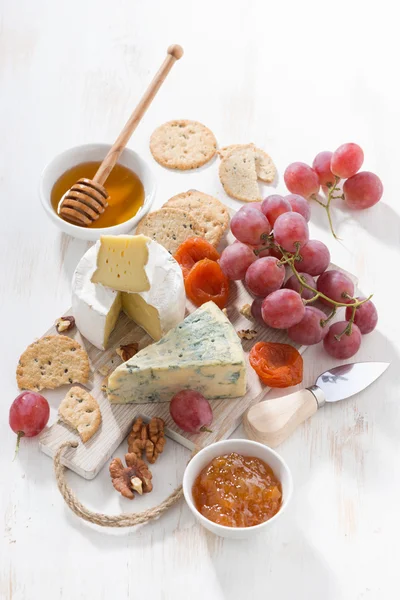 Gjuten ostar, frukt och snacks på en vit träplatta — Stockfoto