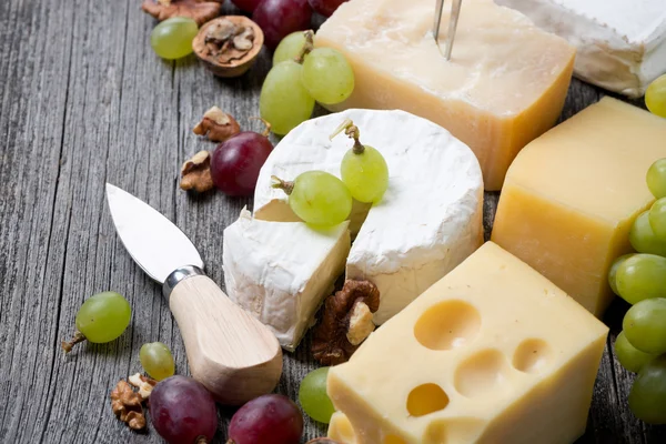 Different cheeses, grapes and walnuts on a wooden background — Stock Photo, Image