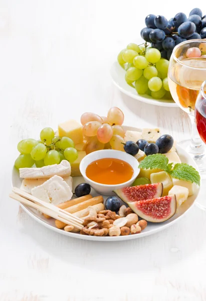cheeses, fruits, wine and snacks on plate, vertical