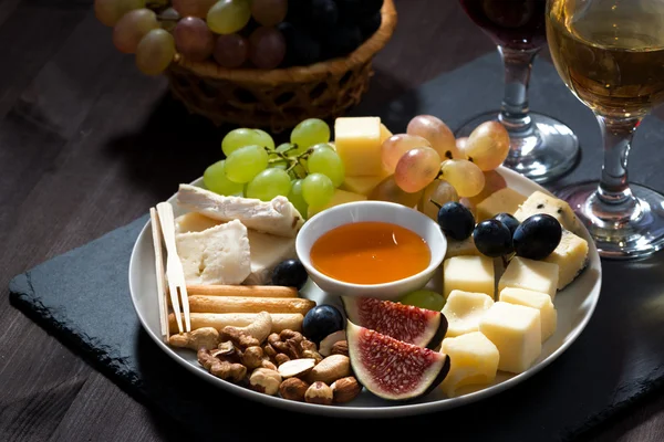 Plate with deli snacks and wine on a dark background, closeup — Stock Photo, Image