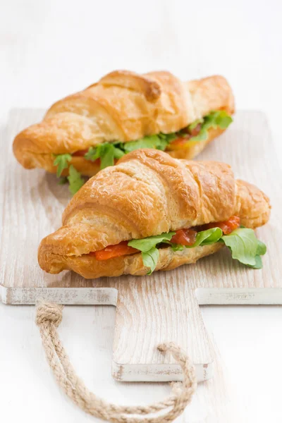 Fresh croissant stuffed with fish and arugula on wooden board — Stock Photo, Image