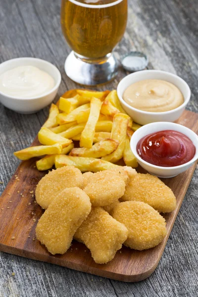 Pepitas de pollo con papas fritas, diferentes salsas y un vaso — Foto de Stock