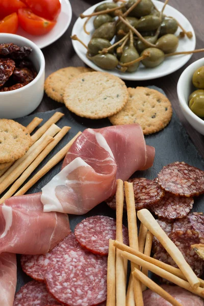 Assorted meat snacks and pickles on a blackboard, close-up — Stock Photo, Image