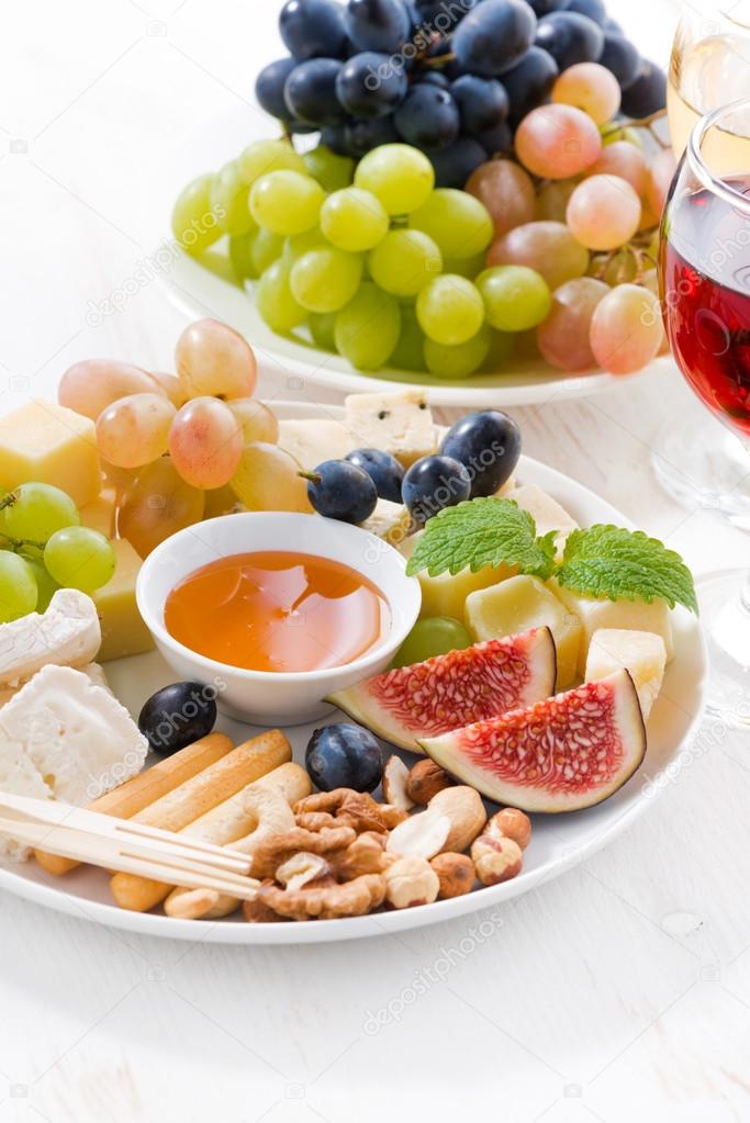 cheeses, fruits, wine and snacks on plate, vertical closeup