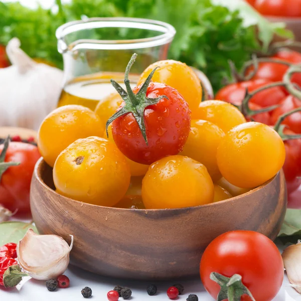 Yellow and red cherry tomatoes in wooden bowl, olive oil, herbs — Stock Photo, Image