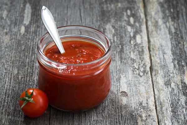 Tomato sauce in a glass jar on a wooden background, closeup — Stock Photo, Image