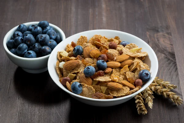 Copos de cereales con arándanos y nueces en una mesa de madera oscura — Foto de Stock