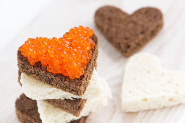Brindes com caviar vermelho em forma de coração na placa de madeira, close-up — Fotografia de Stock