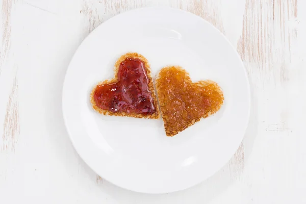 Toasts in heart shape with fruit jam on plate, top view — Stock Photo, Image