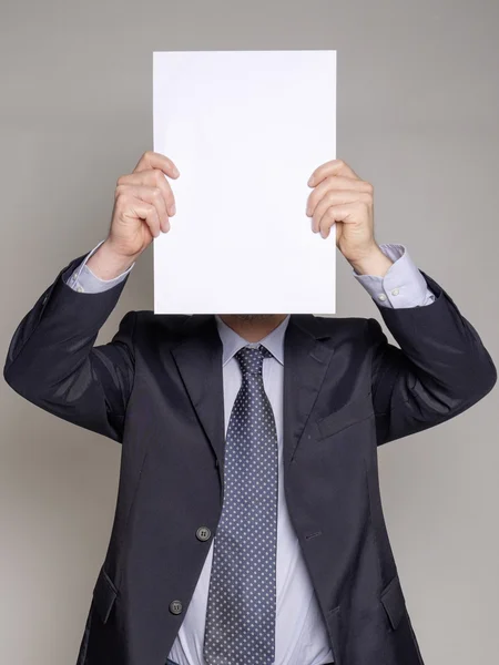 Επιχειρηματίας που κρύβει το πρόσωπό του με μια λευκή copyspace πινακίδα σε γκρίζο φόντο — Φωτογραφία Αρχείου