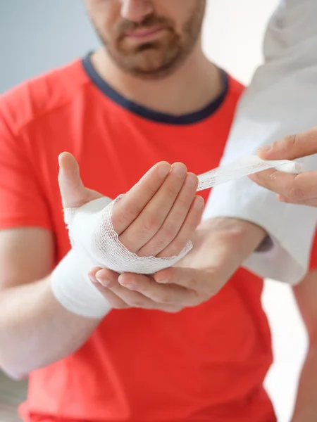 Médico bandaging a mão de um homem do esporte após um acidente — Fotografia de Stock