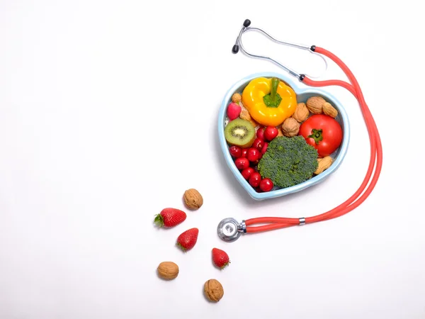 Heart shaped dish with vegetables and stethoscope isolated on white background — Stock Photo, Image