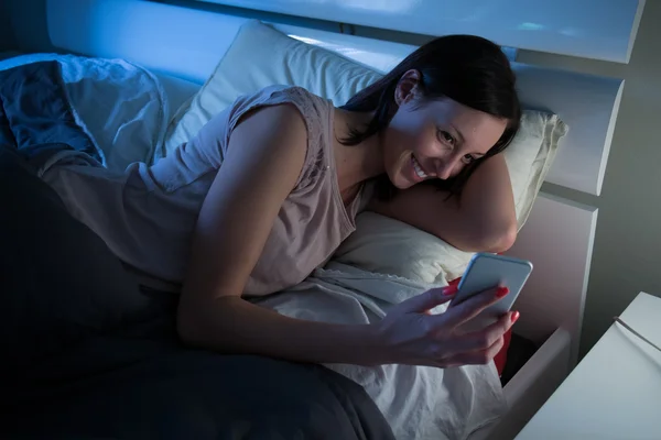Женщина в постели с мобильным телефоном в руке — стоковое фото