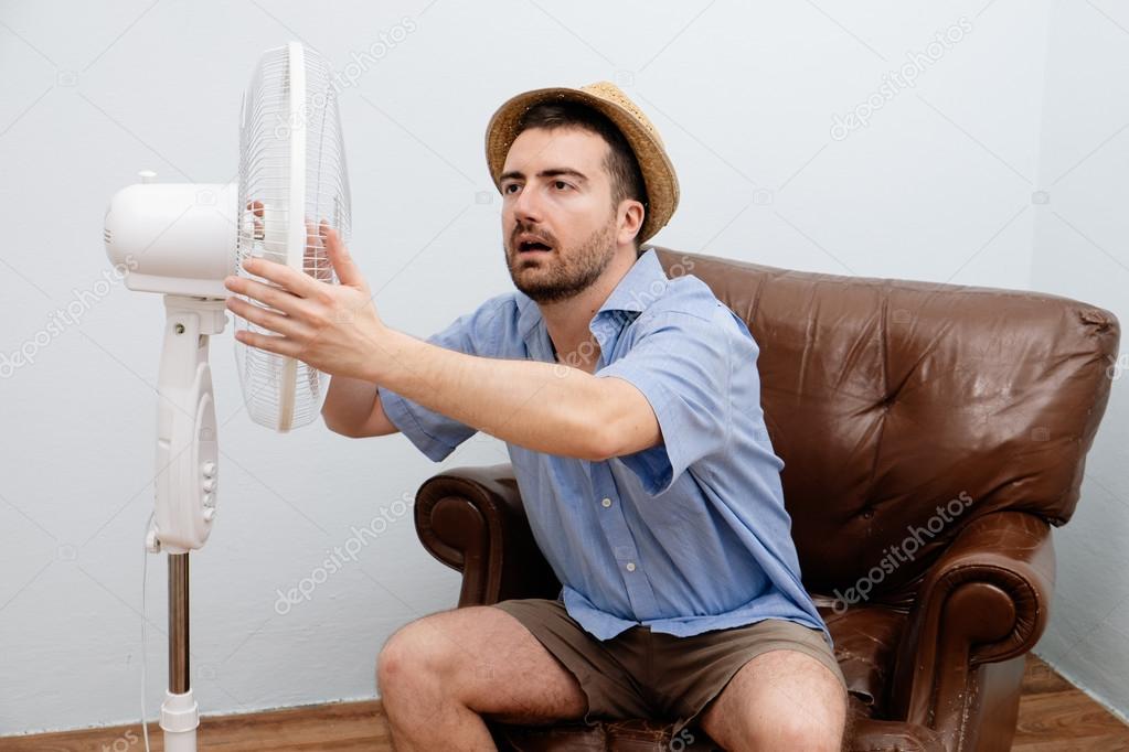 Flushed man feeling hot in front of a fan 