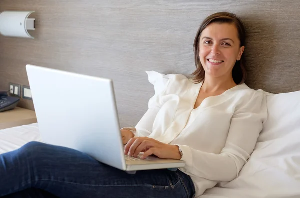 Весела жінка використовує свій ноутбук на ліжку в готелі — стокове фото