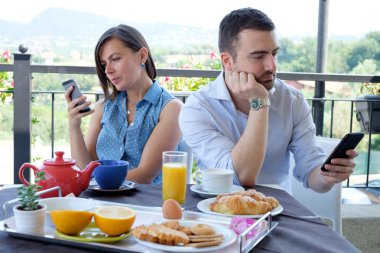 Sıkılmış çift sırasında kahvaltı saati Smartphone kullanarak