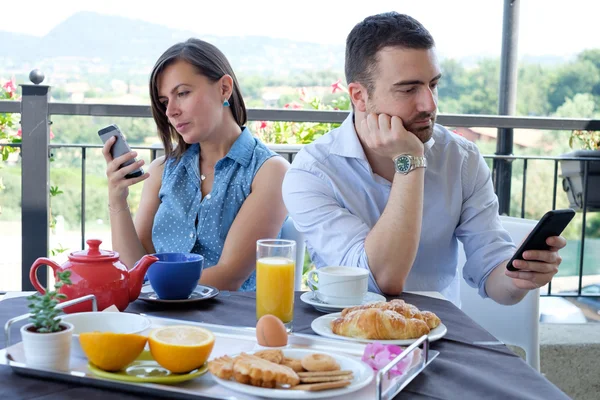 Скучная пара с помощью смартфона во время завтрака — стоковое фото