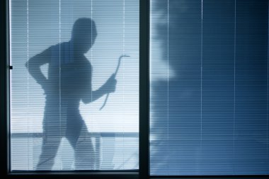 Burglar wearing a balaclava looking through the house window clipart