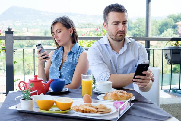 Скучная пара с помощью смартфона во время завтрака — стоковое фото