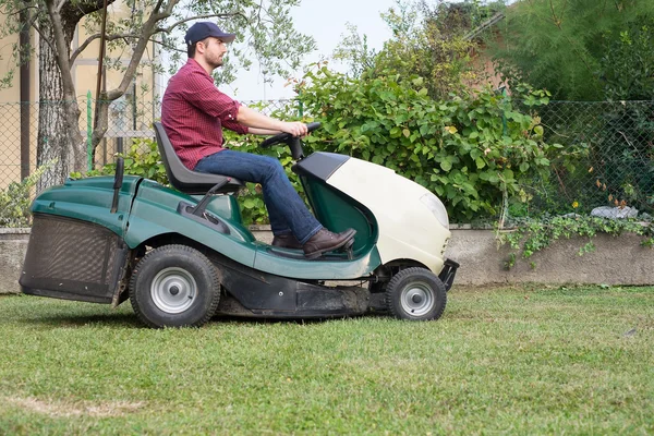 Tuinman snijden het gras van een tuin gezeten op een grasmaaier — Stockfoto