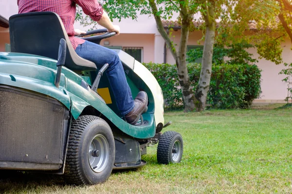 Tuinman snijden het gras van een tuin gezeten op een grasmaaier — Stockfoto