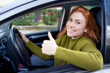 Mutlu kadın yeni arabasını sürüyor, baş parmağını gösteriyor.