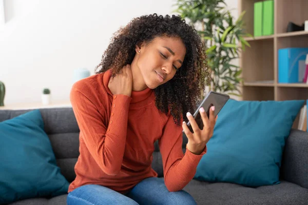Young afro woman suffering from back pain while watching cellphone