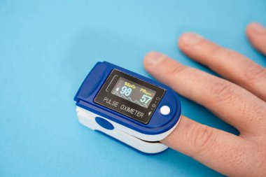 Nabız oksimetresi, parmak dijital aygıtı mavi zemin üzerindeki kanla oksijen doygunluğunu ölçmek için