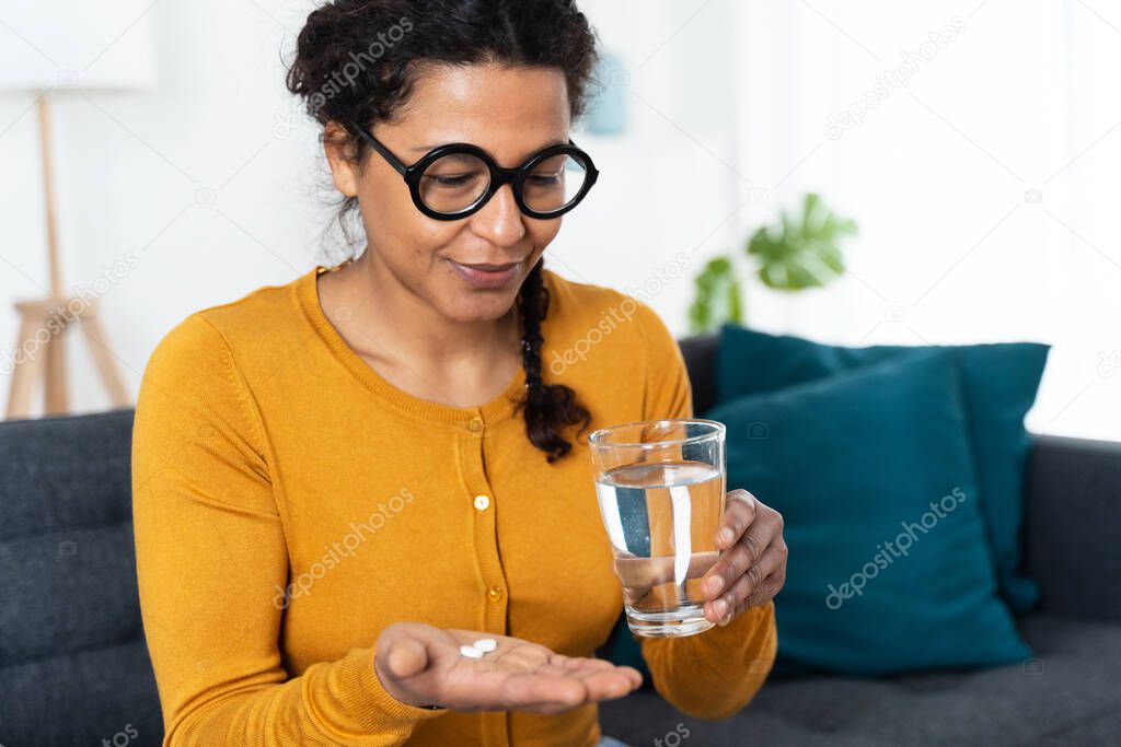 Black woman portrait taking medicine pills at home