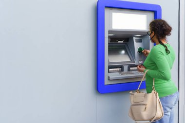 ATM 'den para çekerken koruyucu maske takan siyah bir kadın..