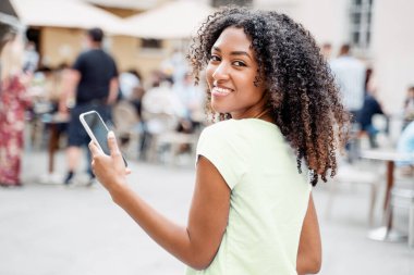 Şehirde cep telefonu kullanan genç siyah bir kadın.