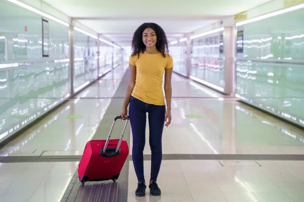 Black woman with cell phone and carry-on baggage in station