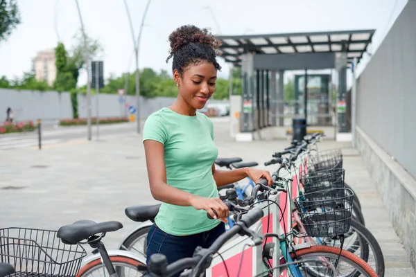 Black woman renting bicycle at public urban cycle transport station