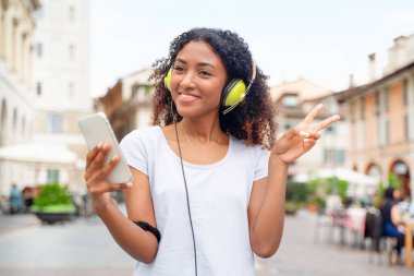 Bir kız akıllı telefon kullanıyor ve sokakta müzik dinliyor.