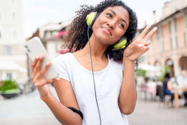 Bir kız akıllı telefon kullanıyor ve sokakta müzik dinliyor.