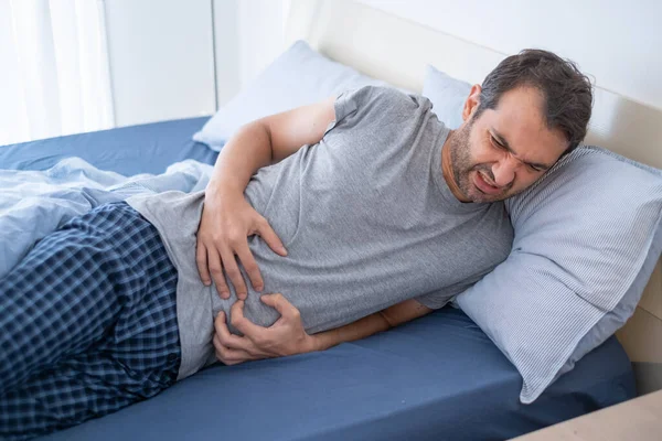 Man in bed suffering from heartburn and stomach pain