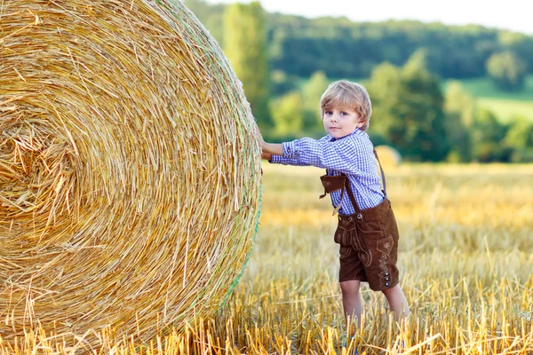 Funny little kid boy in leather shors, walking  through wheat fi — Stock Photo, Image