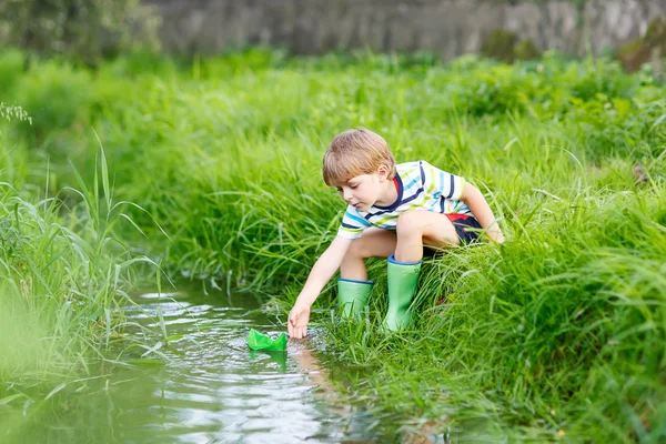 Милый мальчик играет с бумажными лодками у реки — стоковое фото