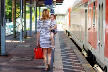 Cute little girl and mother on a railway station. clipart