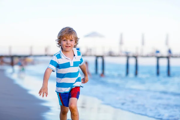 Fröhlicher kleiner Junge, der Spaß daran hat, in oc durch Wasser zu laufen — Stockfoto