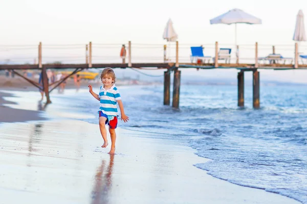 Fröhlicher kleiner Junge, der Spaß daran hat, in oc durch Wasser zu laufen — Stockfoto