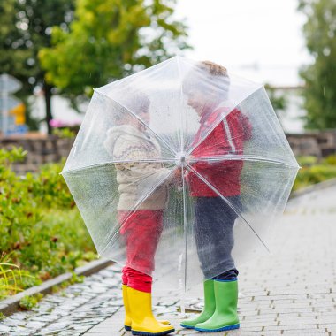 Two little kid boys with big umbrella outdoors