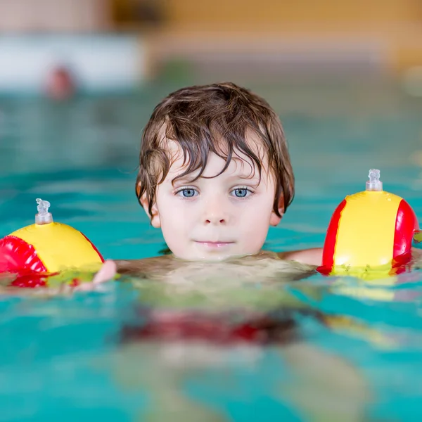 Mały chłopiec dziecko z swimmies uczyć się pływać w krytym basenem — Zdjęcie stockowe