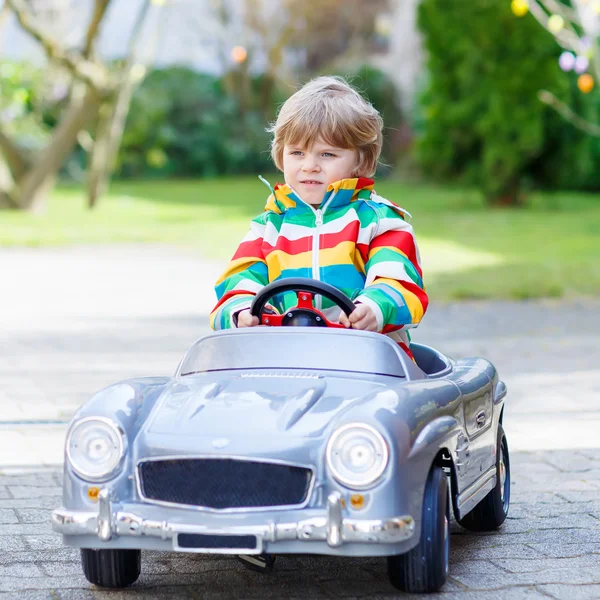 Piccolo bambino in età prescolare guida grande giocattolo vecchia auto d'epoca, all'aperto — Foto Stock